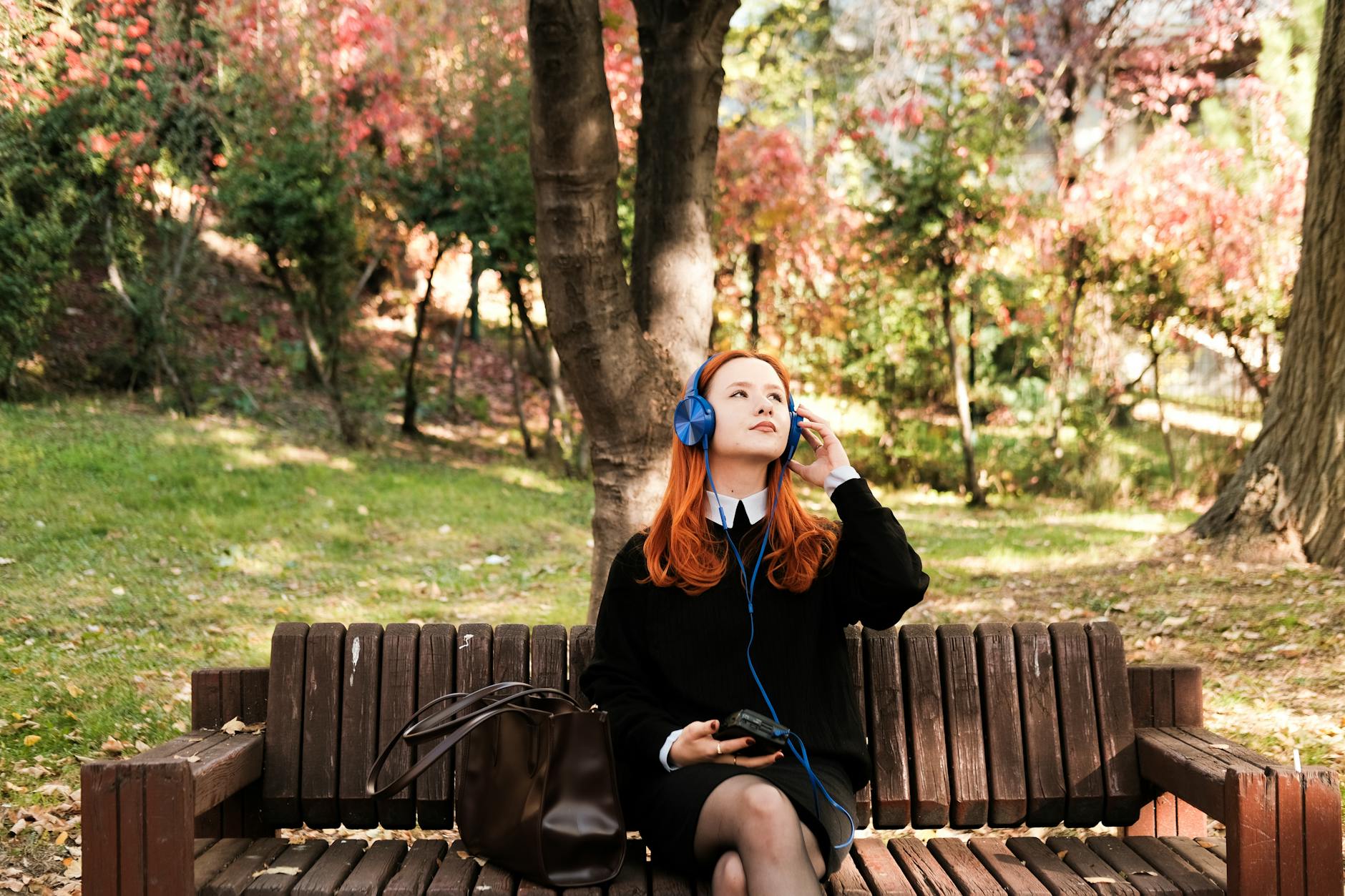 Młoda kobieta na ławce w jesiennym parku słucha muzyki w słuchawkach