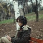 Młody mężczyzna na ławce w jesiennym parku słucha muzyki w słuchawkach