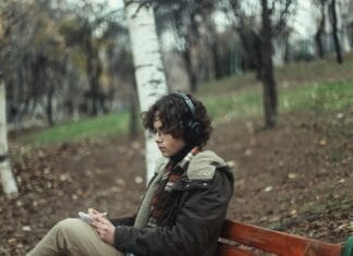 Młody mężczyzna na ławce w jesiennym parku słucha muzyki w słuchawkach