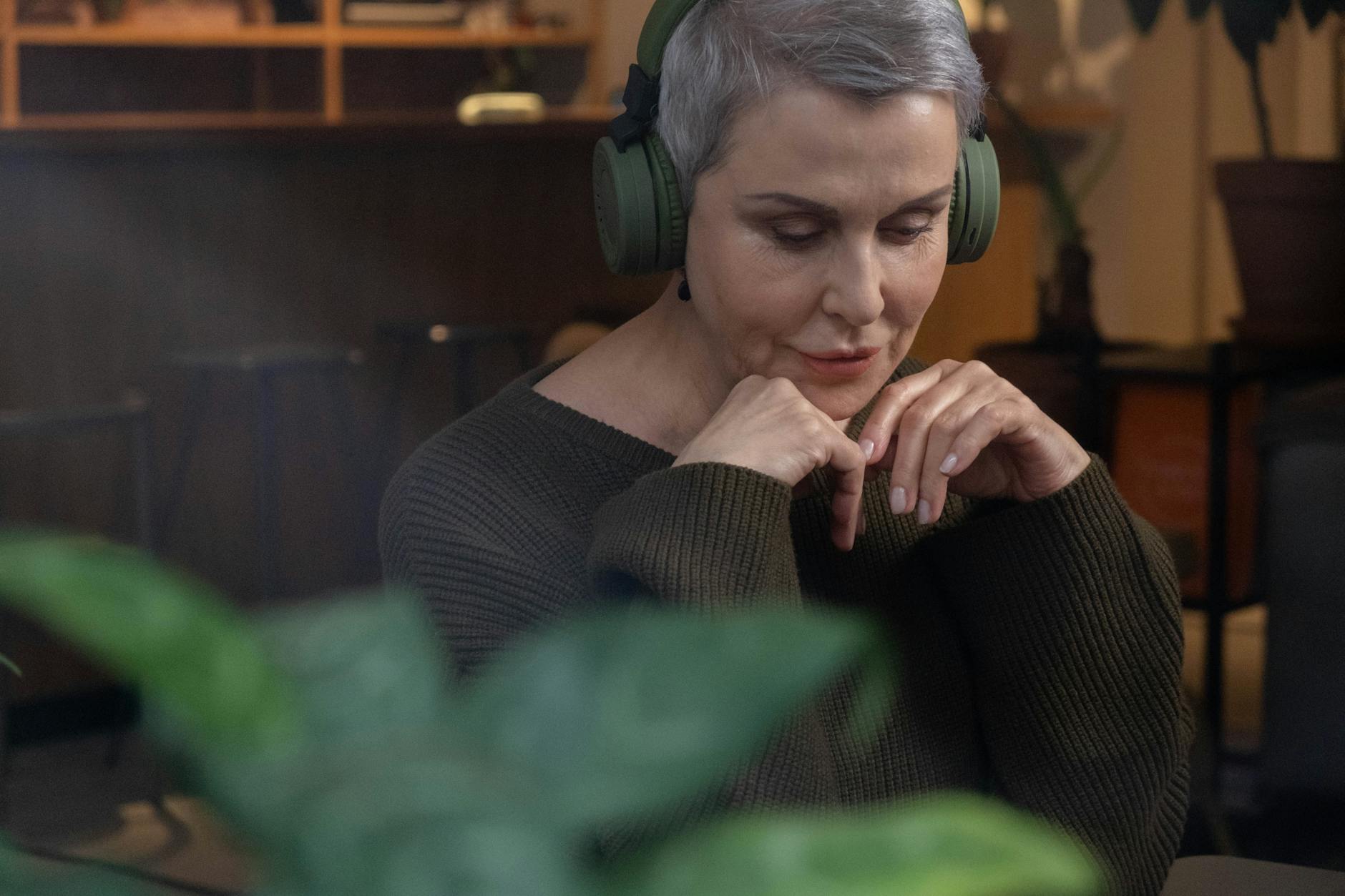 Starsza kobieta w bezprzewodowych słuchawkach relaksuje się w domu