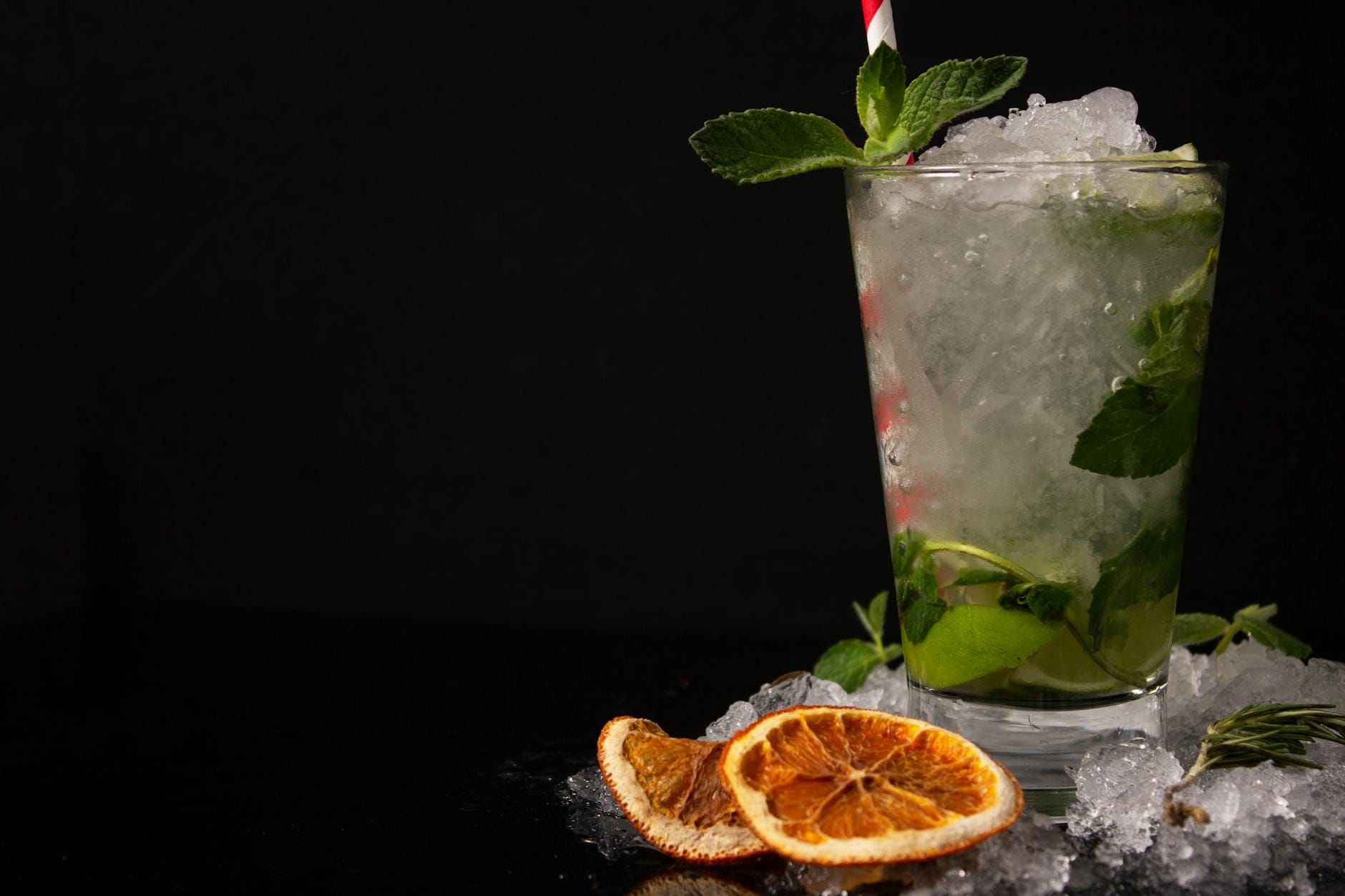 Koktajl mojito z miętą i suszoną pomarańczą na kostkach lodu na czarnym tle