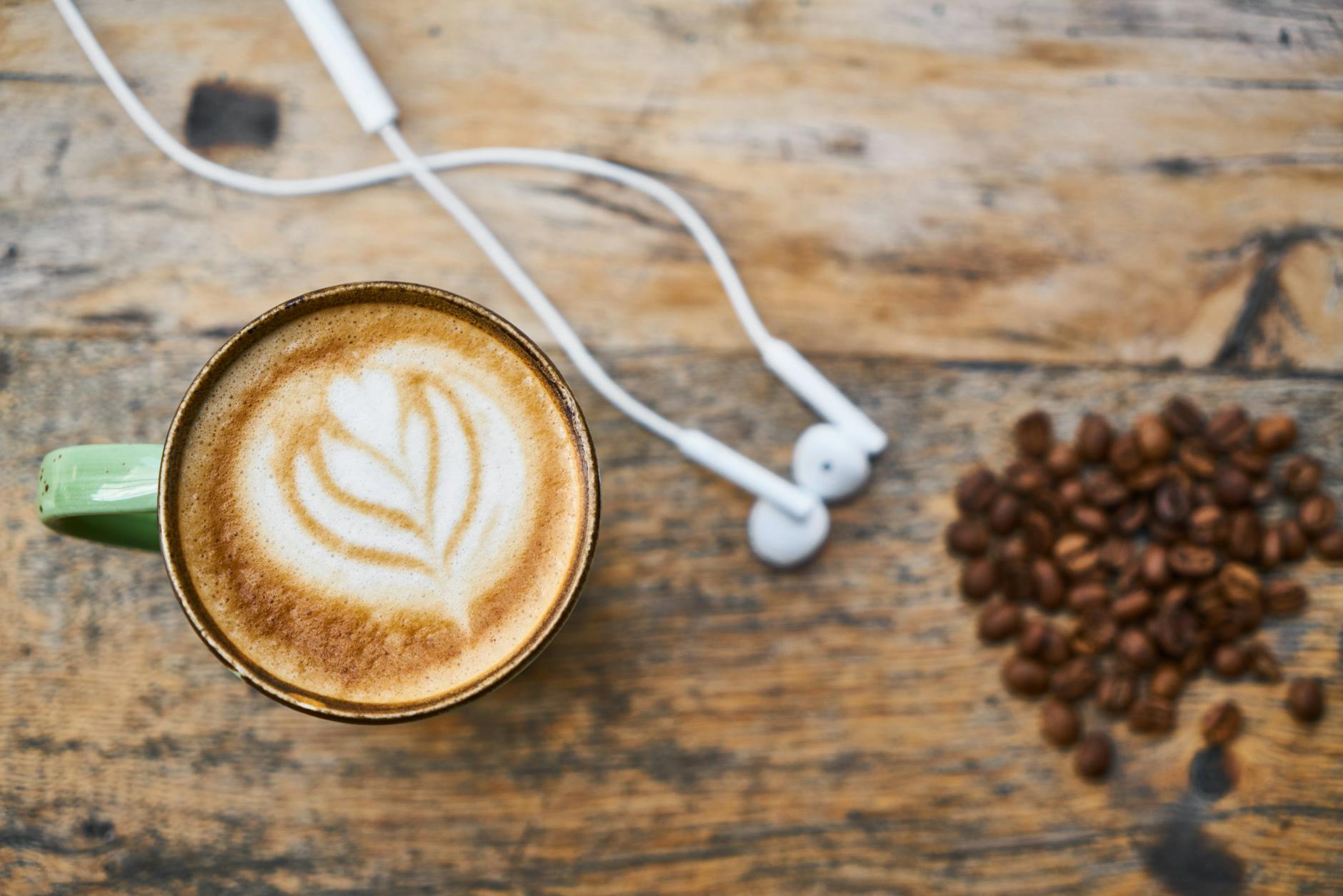 Latte z pianką, słuchawki i ziarna kawy na drewnianym stole