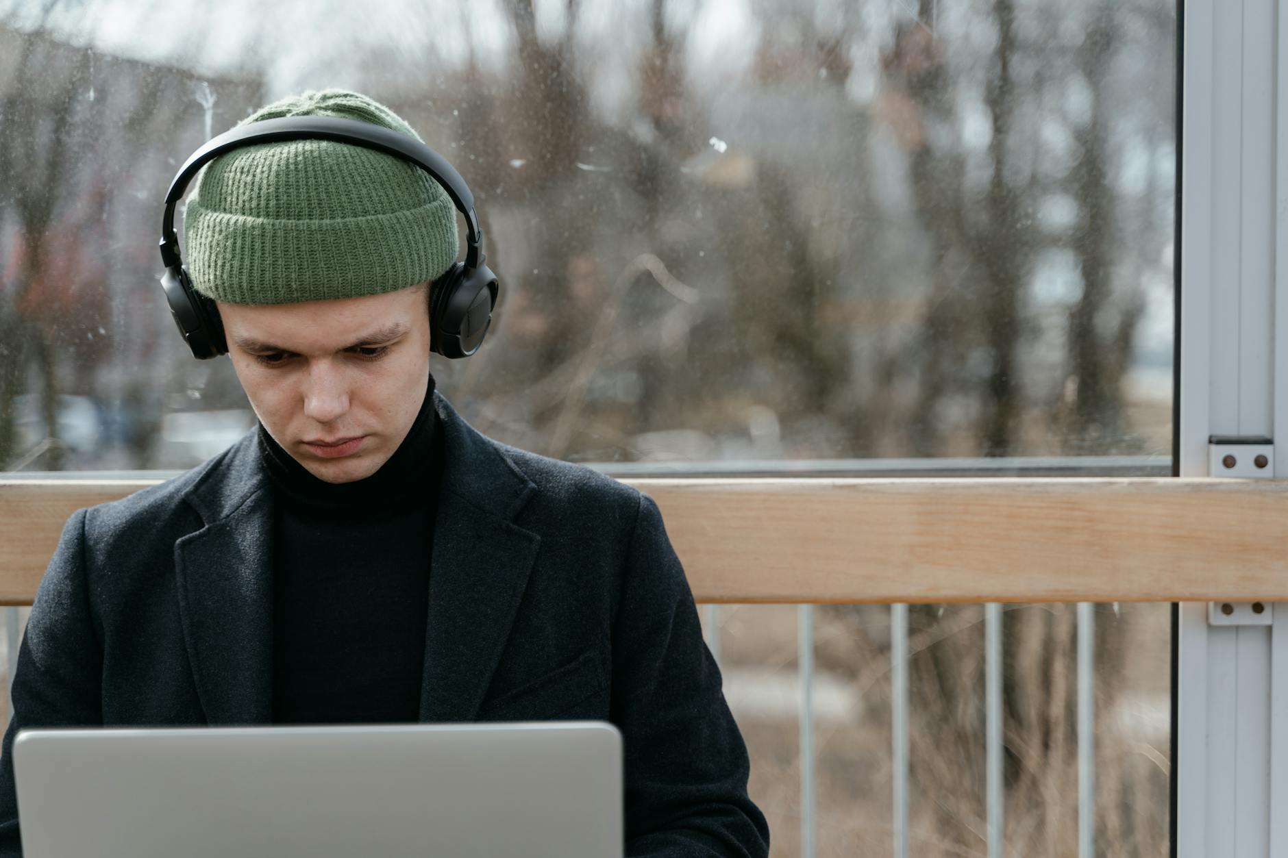 Mężczyzna w zielonej czapce i słuchawkach pracuje na laptopie na zewnątrz