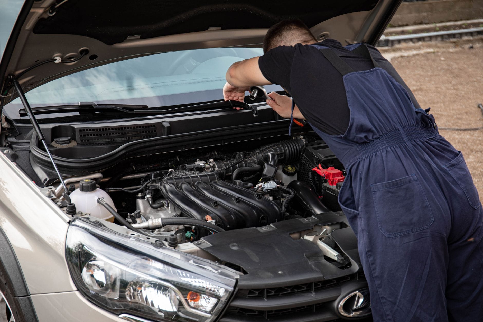 Mechanik w niebieskim kombinezonie naprawia silnik auta na zewnątrz